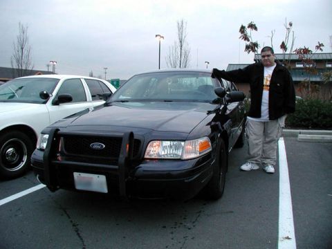 2001 Ford Crown Victoria - A man stands beside a black Ford Crown Victoria, possibly a police vehicle, with another white Crown Victoria in the background.