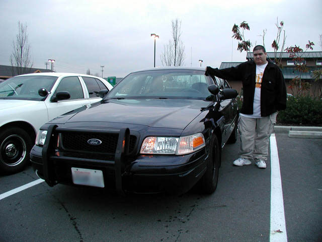Black Ford Crown Victoria police sedan with push bar and pillar spotlight in a parking lot