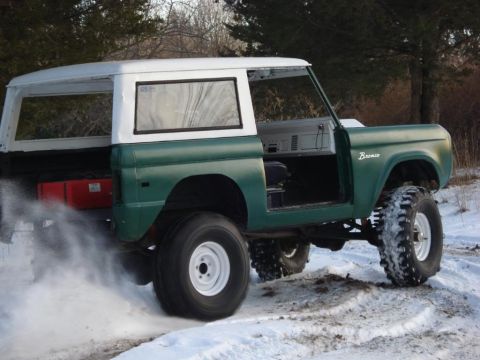 1974 Ford Bronco - A green and white 1974 Ford Bronco with its doors removed drives through the snow.