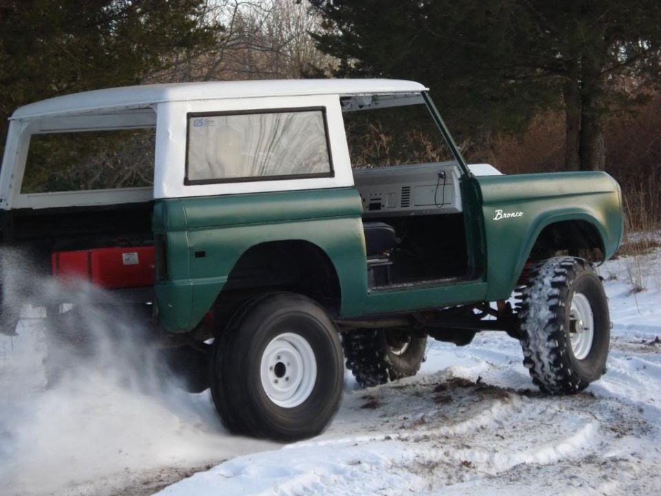 Green and white 1974 Ford Bronco with doors removed, kicking up snow