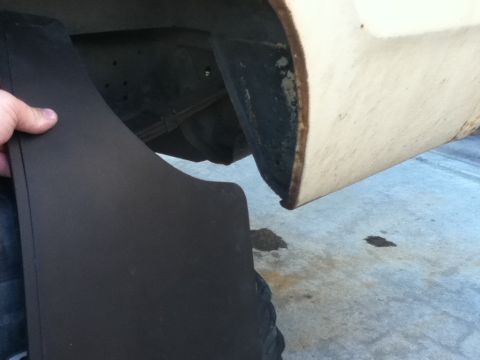 2006 Ford E350 - A person is installing a mud flap on the rear wheel well of a vehicle.