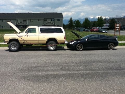 2006 Ford E350 - A beige pickup truck is towing a black coupe, and both vehicles have their hoods open, suggesting mechanical trouble.