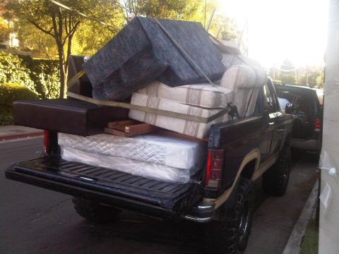 1986 Ford Bronco - A Ford Bronco carries a load of furniture and mattresses, with another vehicle visible behind it.