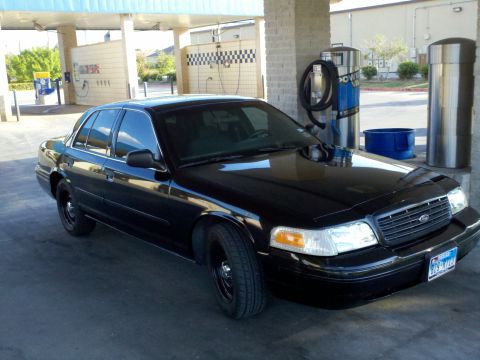 2000 Ford Crown Victoria - A black Ford Crown Victoria is parked under a canopy at a car wash, with a vacuum cleaner to its right.