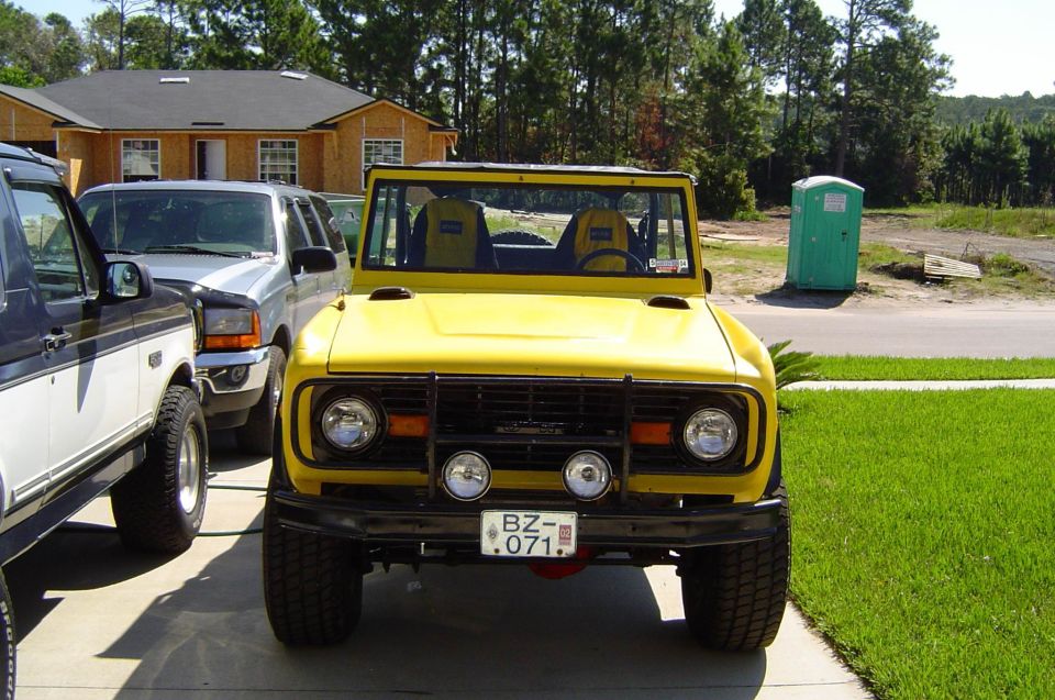 Yellow Ford Bronco, front view, black brush guard with driving lights, on driveway