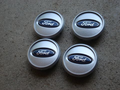 2000 Ford Crown Victoria - Four Ford center caps are displayed on a textured gray surface.