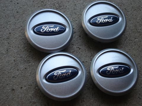 2000 Ford Crown Victoria - Four silver Ford center caps with blue Ford oval logos are displayed on a concrete surface.