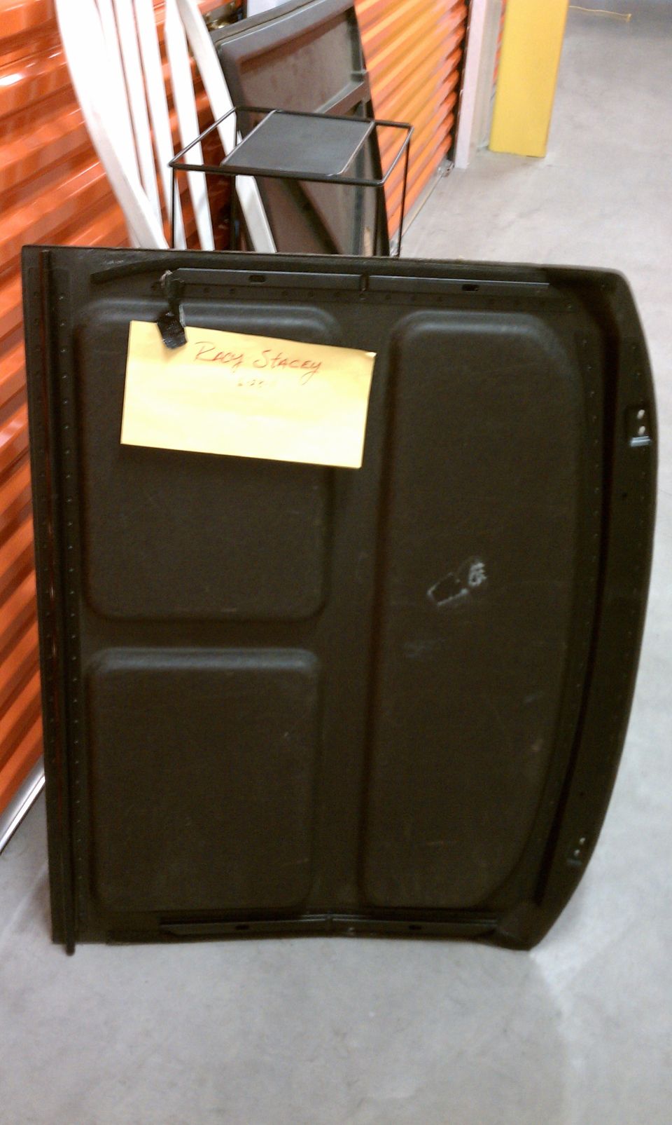 Underside of a black steel hood panel tagged "Racy Stacey" in a storage unit hallway