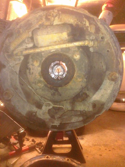 1995 Ford Bronco - Close-up of a heavily corroded vehicle brake drum assembly, supported by jack stands in a workshop environment.