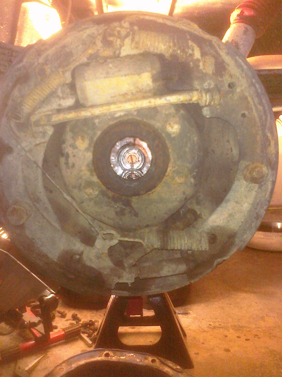 Rusty brake drum assembly on jack stands, showing a central hub and surrounding components