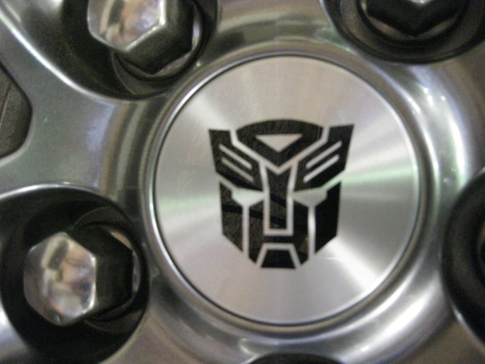 Silver wheel hubcap with black Transformers Autobot logo and Supermotors.net text