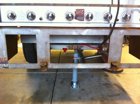 1987 Suzuki Samurai - Undercarriage view of a trailer frame, a grill and a visible tire, with a jack stand supporting it.