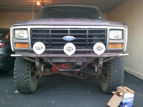 1982 Ford Bronco - The front end of a 1982 Ford Bronco is shown, a custom bumper and three Hella driving lights mounted above it.