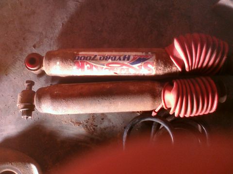 1995 Ford Bronco - Two rusty shock absorbers with red bellows are shown, one with a brand sticker.