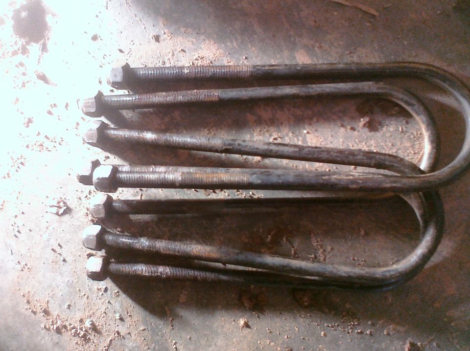 Several rusty U-bolts with nuts on a concrete surface