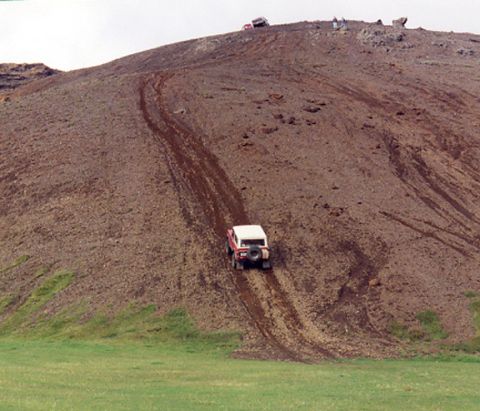 1974 Ford Bronco - Off-road vehicles navigate a challenging dirt incline under an overcast sky.
