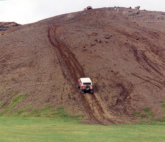 White-topped SUV climbing a steep muddy rutted hillside