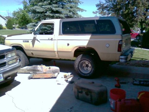 2006 Ford E350 - A tan Dodge Ramcharger with a camper shell is parked outside with parts and tools scattered around it.