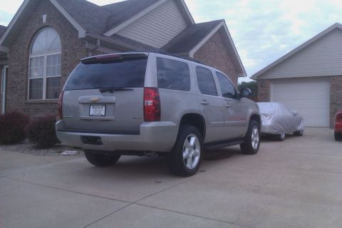 2007 Chevrolet Tahoe - The rear of a silver Chevrolet Tahoe is visible, parked in front of a brick house and garage.