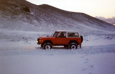 1974 Ford Bronco - A 1974 Ford Bronco drives through a snowy landscape with mountains in the background.