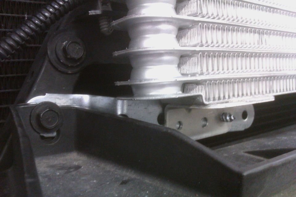 Close-up of a vehicle's radiator or oil cooler assembly with visible mounting brackets and bolts