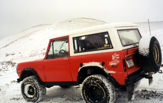 Red and white lifted Ford Bronco on a snowy hill with rear-mounted spare tire