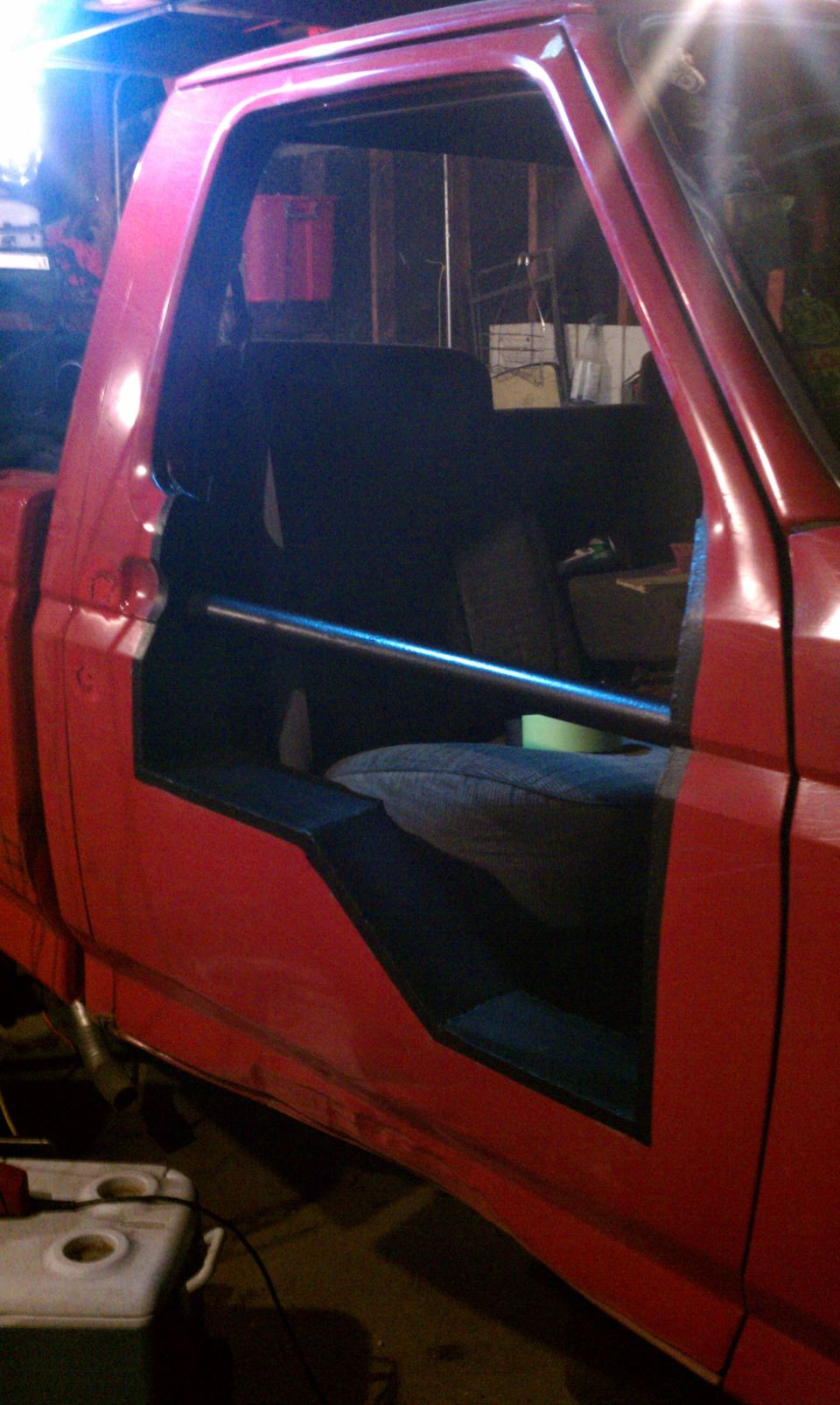 Red pickup truck interior with roll bar, door removed, showing seats and dashboard