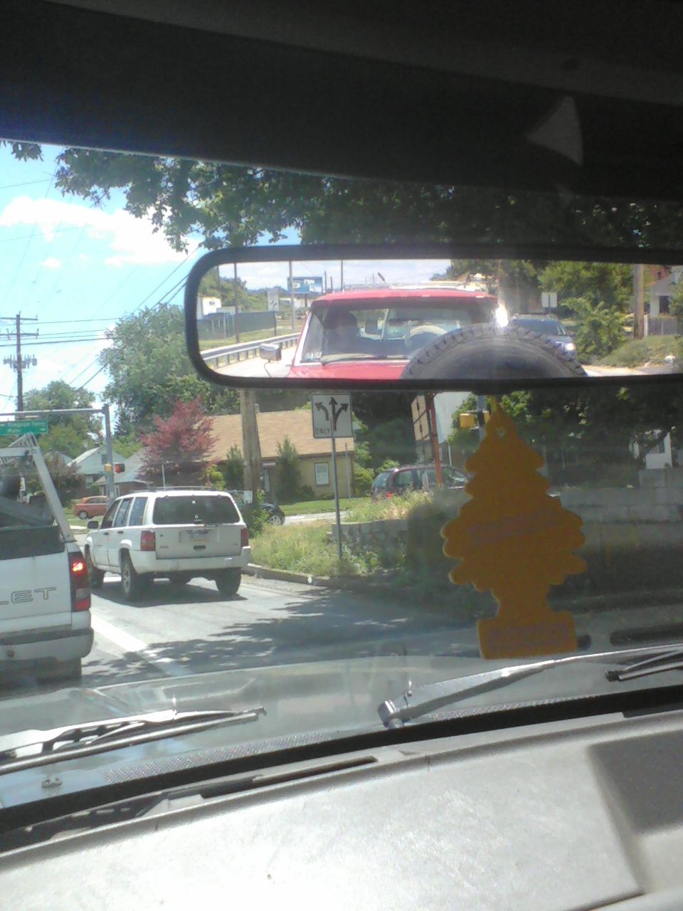 Red SUV with spare tire mounted on rear door, seen in rearview mirror. White SUV and white truck also visible