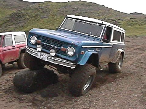 1974 Ford Bronco - A blue 1974 Ford Bronco navigates rough terrain with another Bronco in the background.