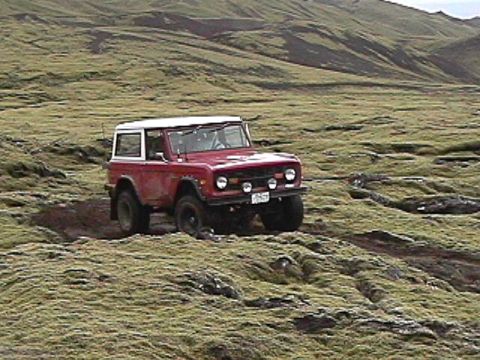 1974 Ford Bronco - A red SUV navigates a challenging, uneven landscape covered in moss and rocks.