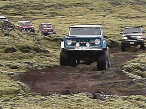 1974 Ford Bronco - A blue 1974 Ford Bronco leads a group of off-road vehicles through a mossy, rocky terrain in Iceland.