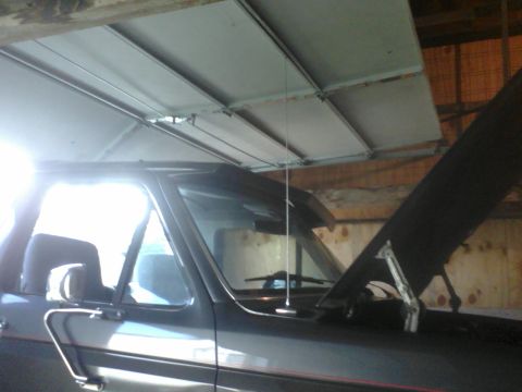 1988 Ford Bronco - 1988 Ford Bronco with hood open, parked indoors. The side profile is visible, including the door and antenna.