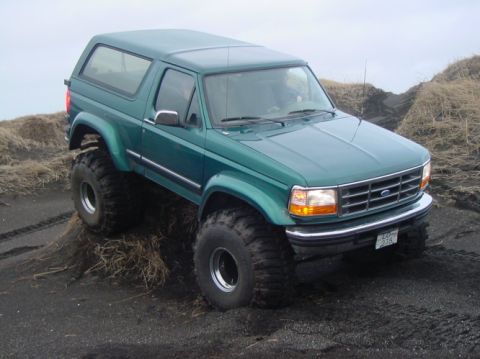 1993 Ford Bronco - A modified green Ford Bronco navigates a rough, muddy terrain with large off-road tires.