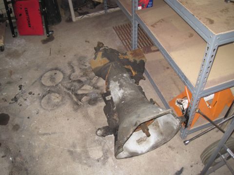1979 Ford Bronco - A transmission part rests on a concrete floor in a garage setting, with shelving and tools visible in the background.