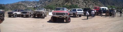 1982 Ford Bronco - A collection of modified off-road vehicles are gathered in a dusty outdoor area.
