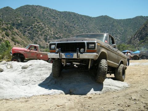 1982 Ford Bronco - Two lifted pickup trucks are navigating a rocky, off-road terrain under a clear blue sky.
