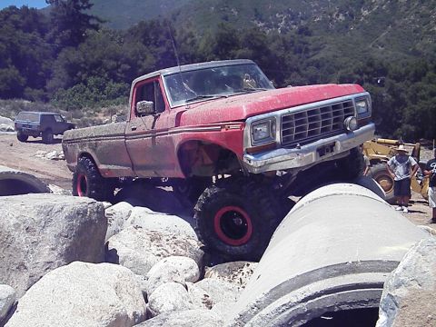 1982 Ford Bronco - A lifted 1979 Ford F-Series pickup truck navigates a challenging off-road course with large rocks and concrete pipes.