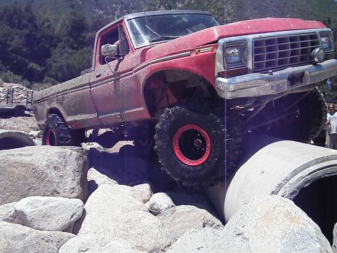 1982 Ford Bronco - A lifted red pickup truck navigates a rocky obstacle course with large concrete pipes.