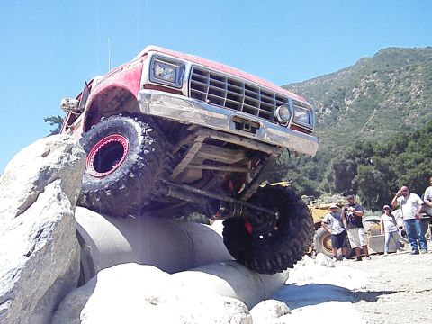 1982 Ford Bronco - A red off-road truck navigates a rocky obstacle course with spectators watching.