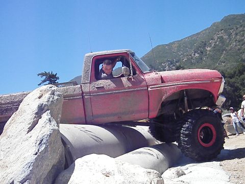 1982 Ford Bronco - This lifted pickup truck is shown off-roading over large concrete pipes and rocks.