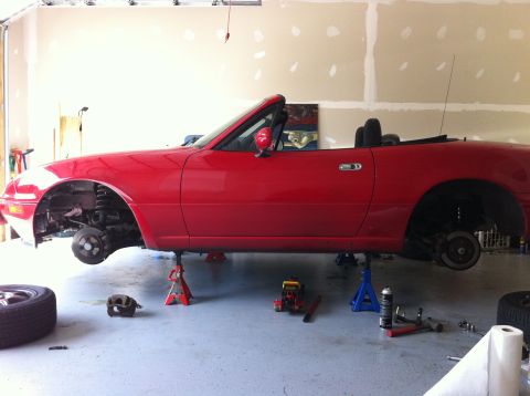 1990 Mazda Miata - A red Mazda Miata is elevated on jack stands in a garage, with its wheels off for service.