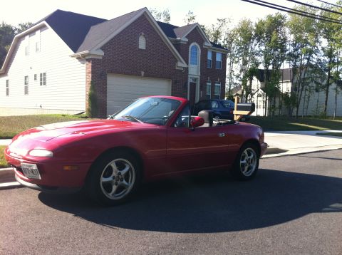 1990 Mazda Miata - A red 1990 Mazda Miata convertible is parked in front of a brick house on a sunny day.