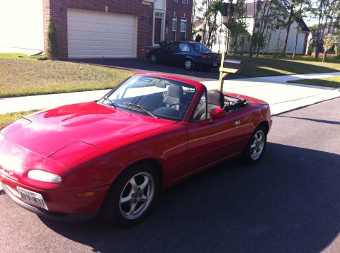 1990 Mazda Miata - A red 1990 Mazda Miata convertible is parked on a suburban street, with another car in the background.