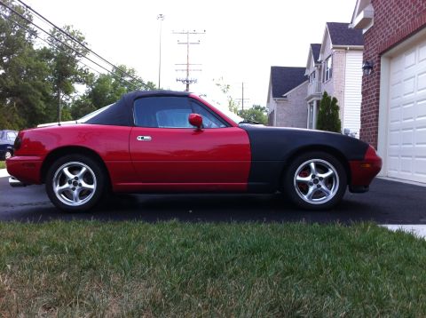 1990 Mazda Miata - This red and black convertible sports car is parked in a driveway with houses in the background.