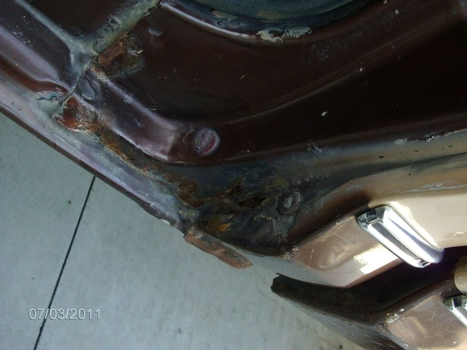 Brown vehicle door jamb with significant rust and damage. Chrome door handle visible