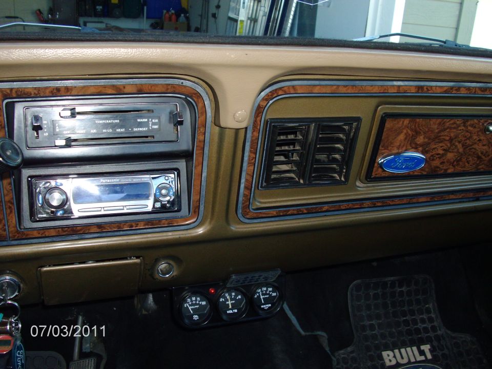 Dashboard with wood grain trim, aftermarket stereo, and climate controls. Also has a Ford emblem and auxiliary gauges