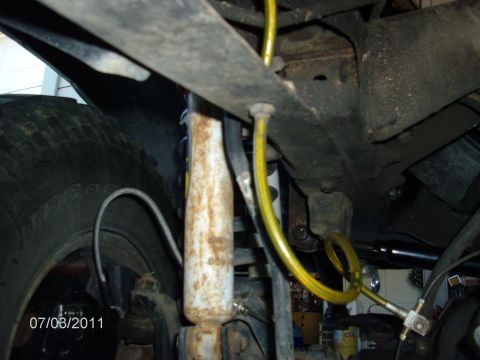 1979 Ford F-150 - A close-up shot reveals the undercarriage of a vehicle, focusing on a yellow hose and a rusty shock absorber.