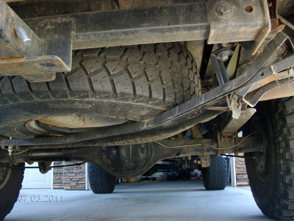 Undercarriage view of a truck showing the spare tire mounted underneath, leaf springs, and rear differential