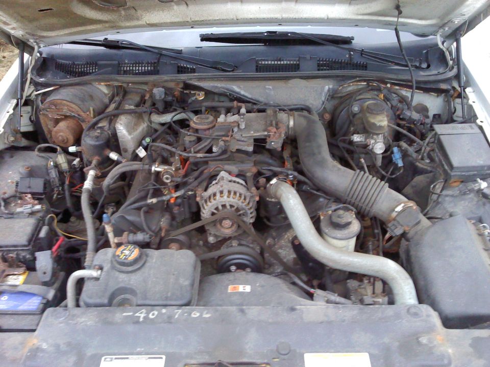 Engine bay with V8 engine, hoses, and belts visible. Some writing on the radiator cover
