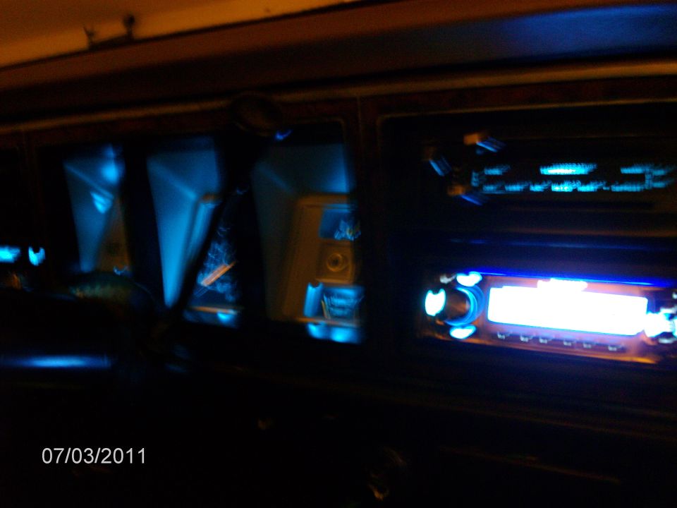 Dashboard interior with blue illuminated gauges and two car stereos, one with a bright screen